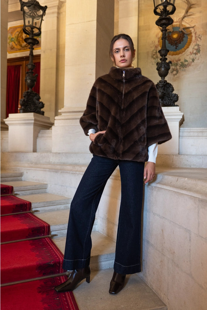 Woman in a brown fur coat standing on a staircase with red carpet