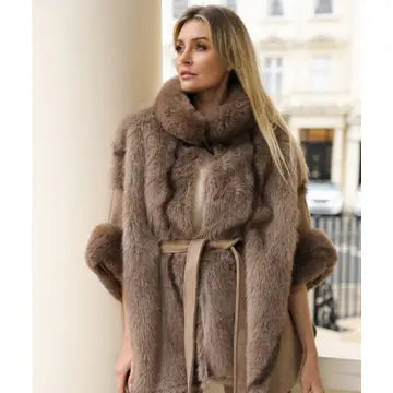 A woman wearing a brown faux fur wrap coat with a matching belt, standing in front of a light-colored building.