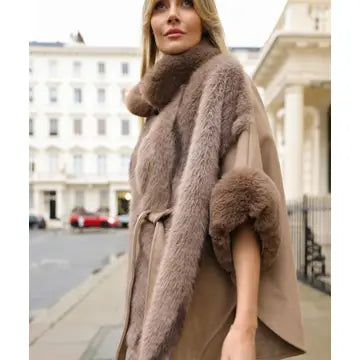 A woman wearing a taupe faux fur coat with a high collar and matching belt, standing on a city street.