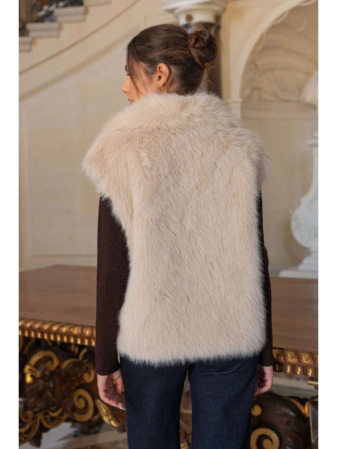 Person wearing a white fur vest in an elegant interior setting