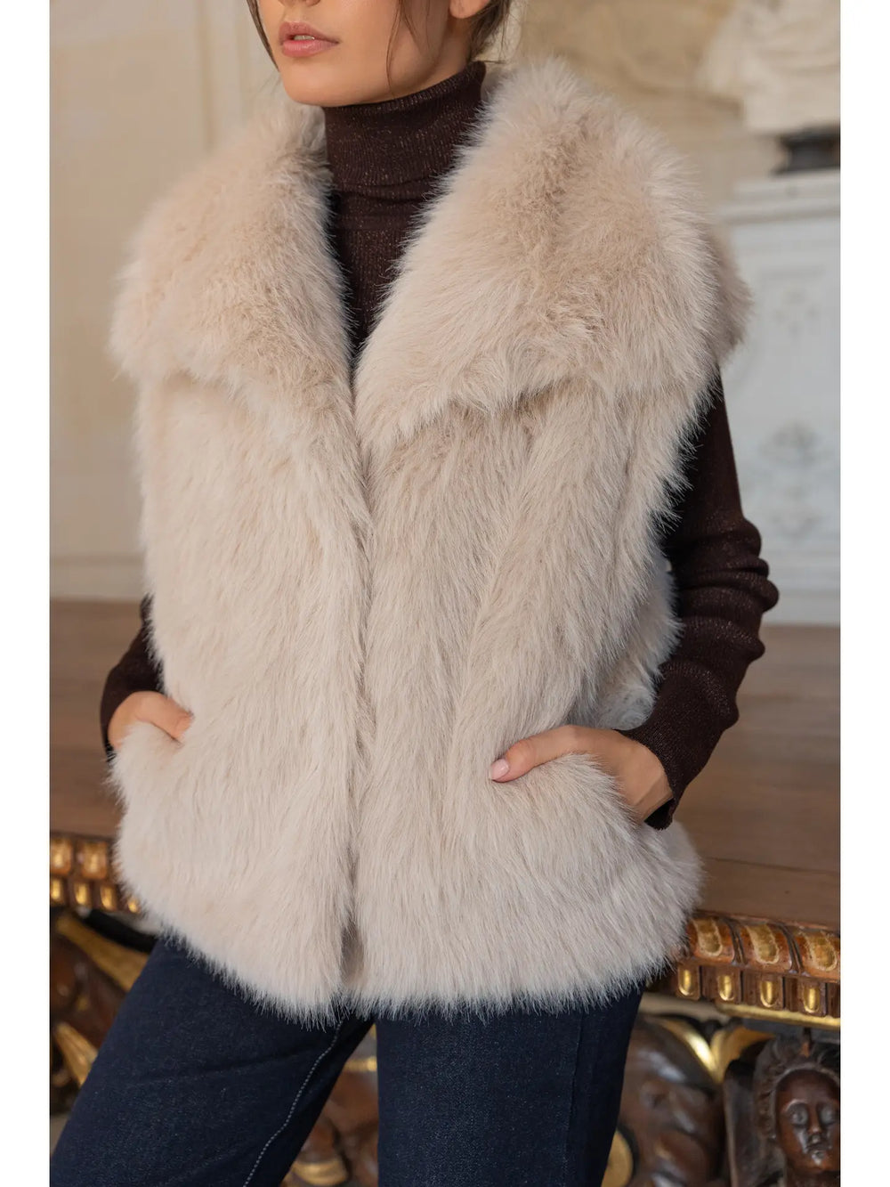 Person wearing a fluffy white fur vest over a dark outfit.