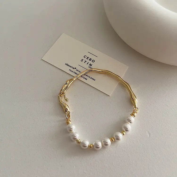 Gold bracelet with pearls on a white surface with a brand tag.