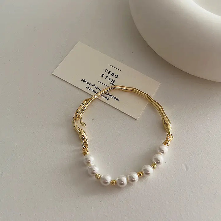 Gold bracelet with pearls on a white surface with a brand tag.