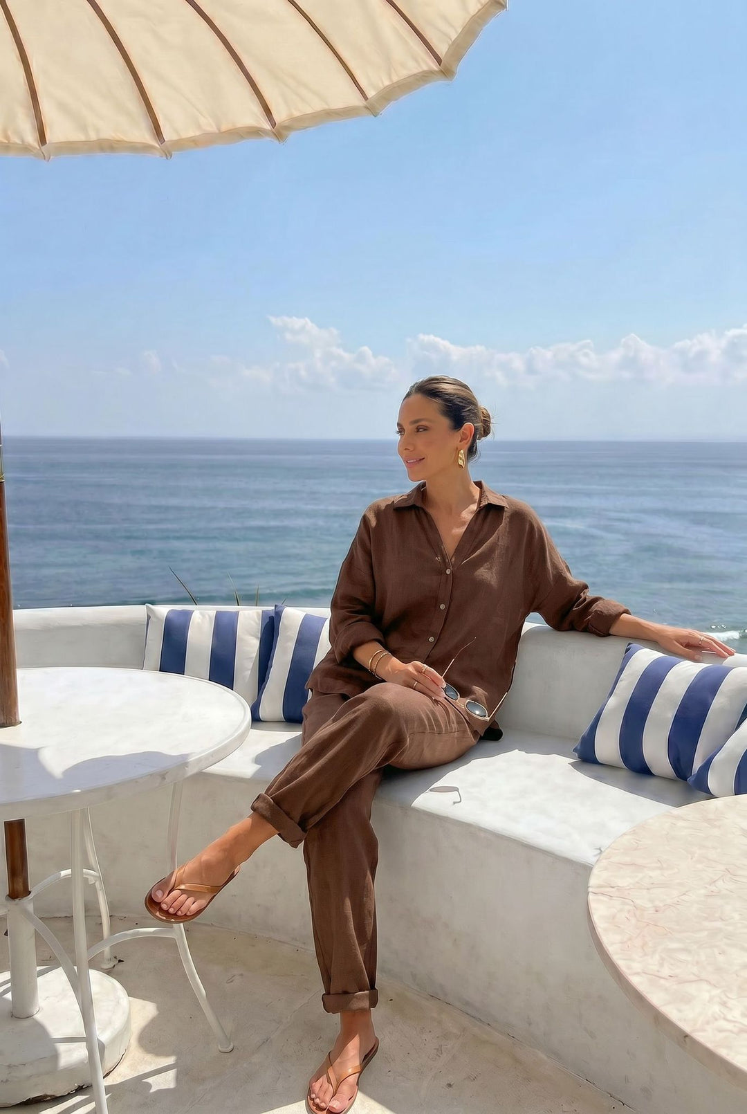 Woman sitting on a white outdoor sofa with blue and white striped cushions, overlooking the ocean.