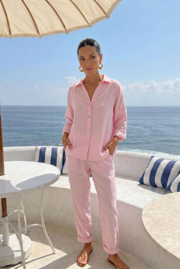 Woman in pink outfit standing by the ocean with a white umbrella and blue and white striped cushions.