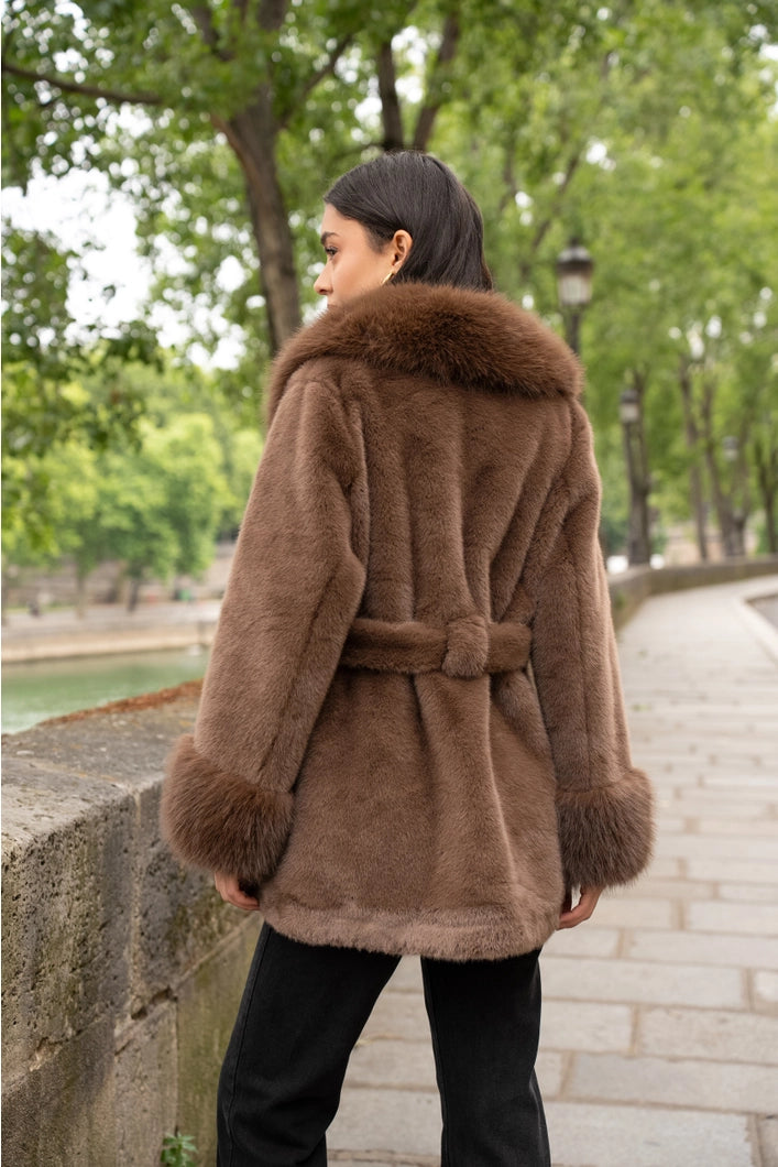 Woman wearing a brown fur coat walking along a tree-lined path.