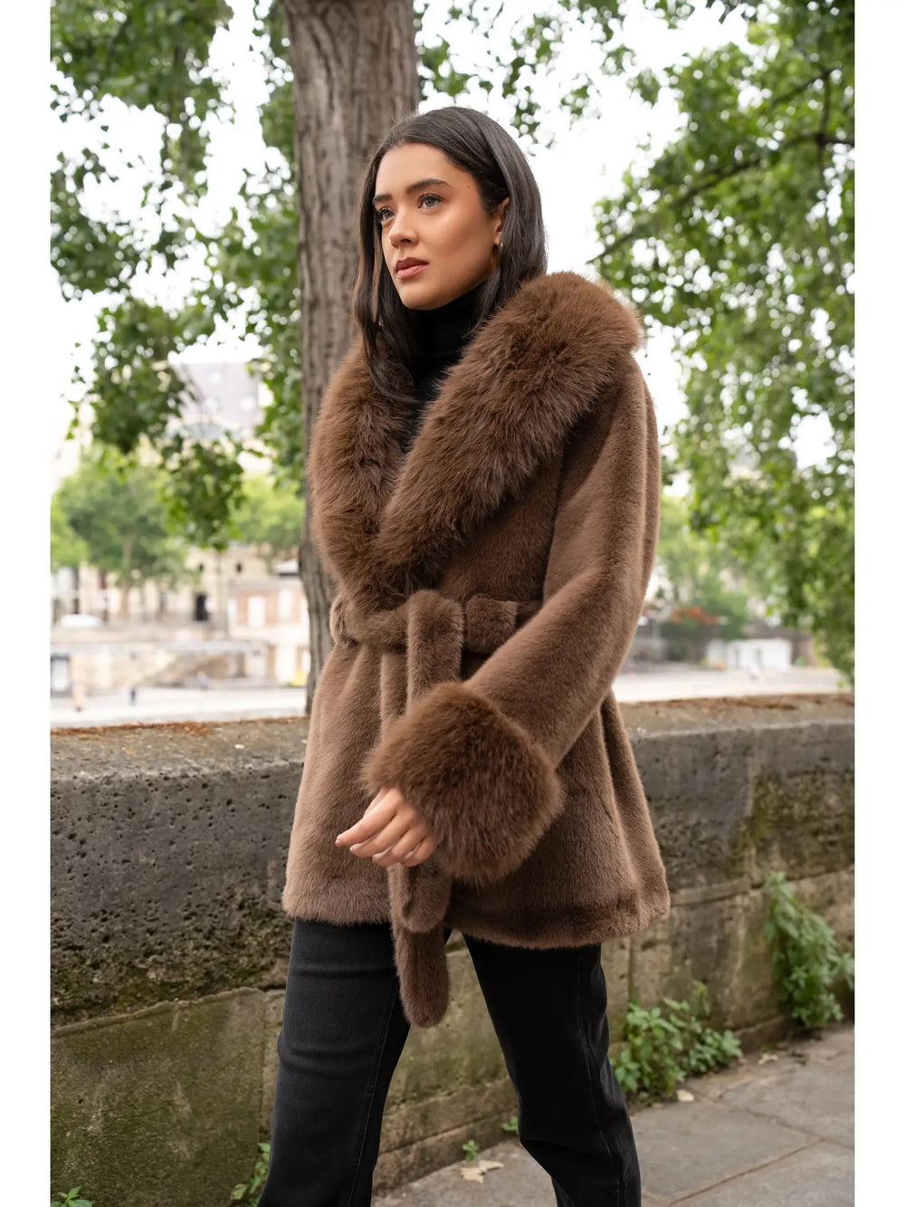 Woman wearing a brown coat with fur trim standing outdoors.