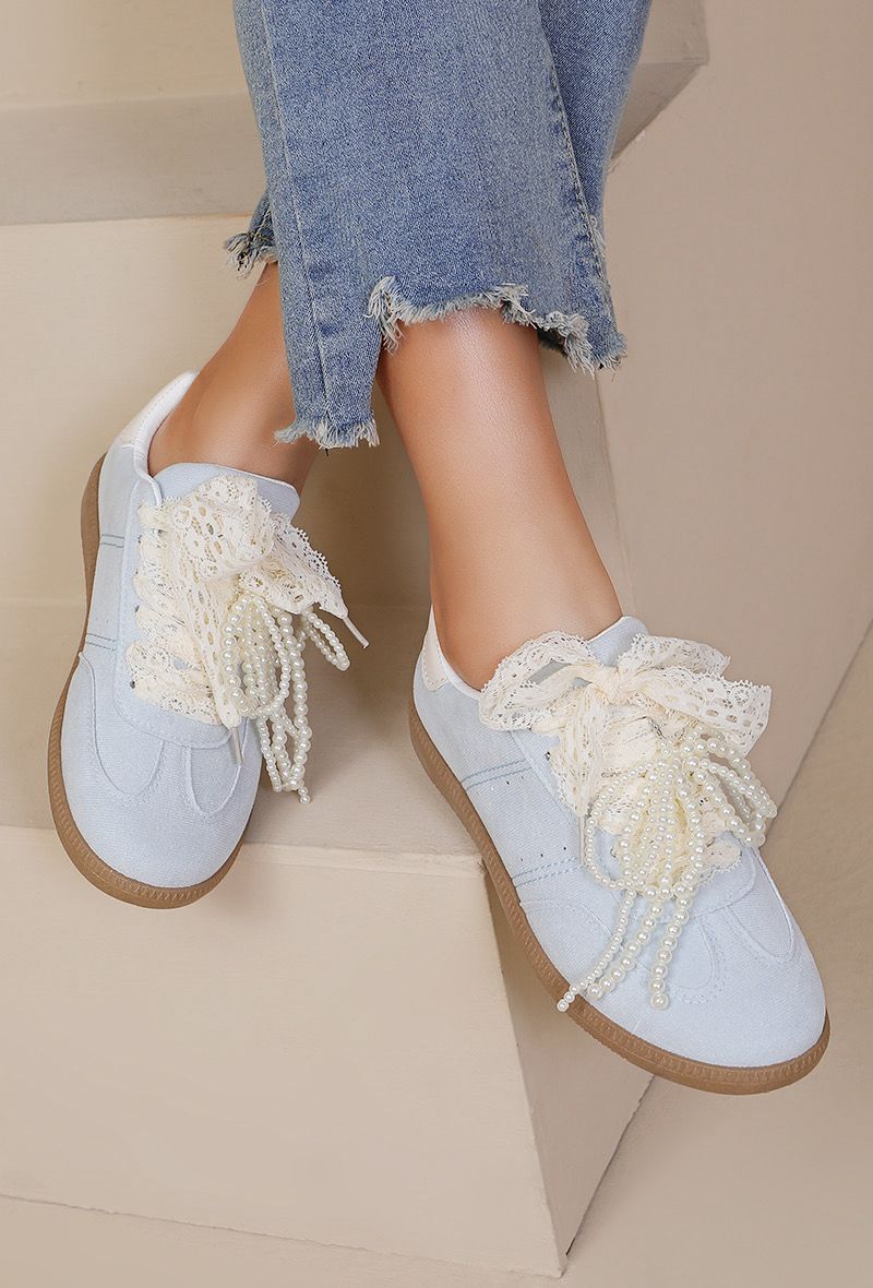 Light blue sneakers with lace details worn with denim jeans on a neutral background