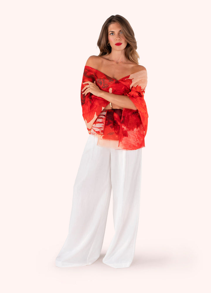 Woman wearing a red floral off-shoulder top and white pants on a white background