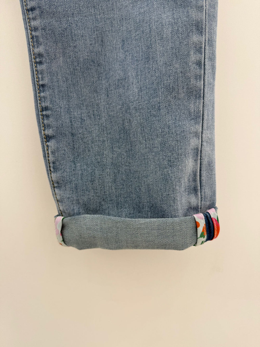 Close-up of rolled-up blue jeans with floral cuffs on a beige background