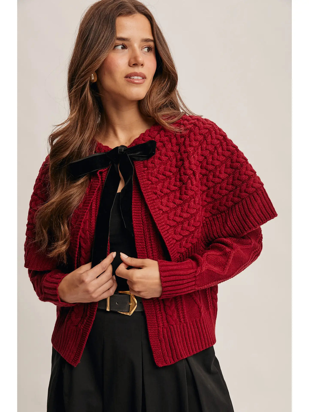 Woman wearing a red knitted cardigan over a black top on a beige background