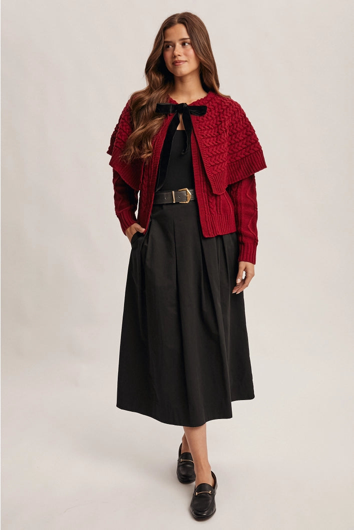 Woman wearing a red knitted cardigan over a black dress on a plain background