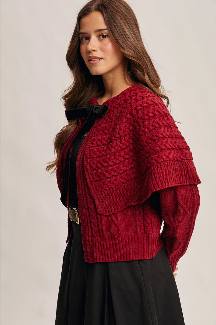Woman wearing a red knitted cardigan over a black top and skirt on a beige background