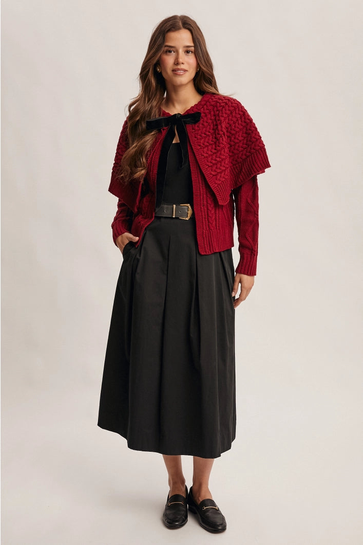 Woman wearing a red knitted cardigan over a black outfit on a plain background