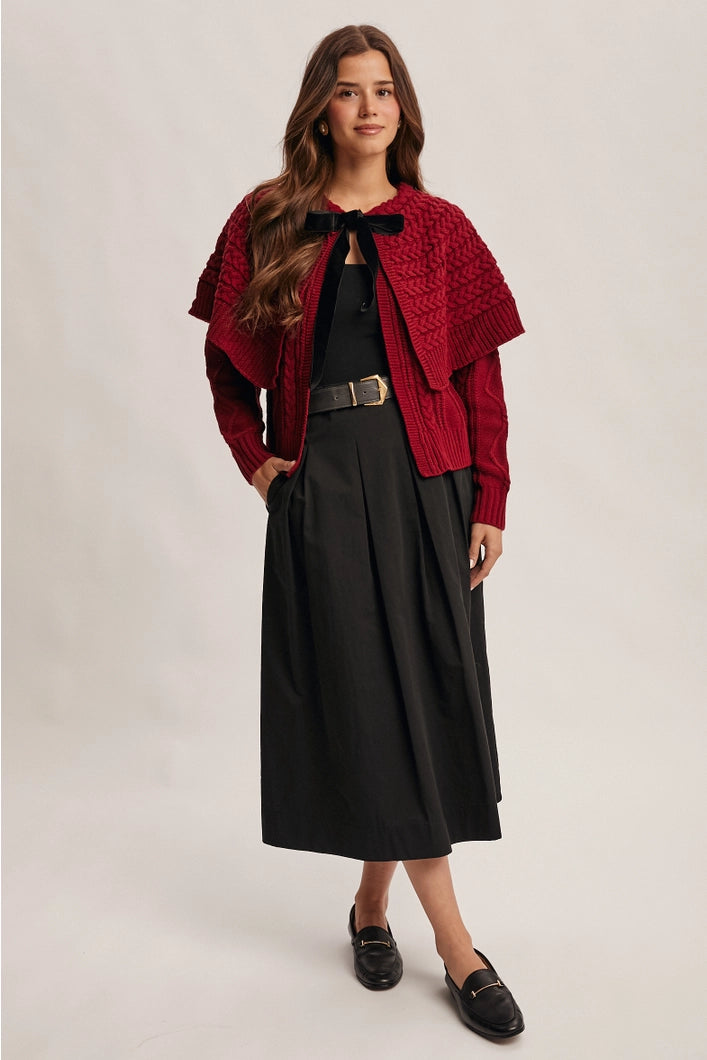 Woman wearing a red knitted cardigan over a black outfit on a plain background