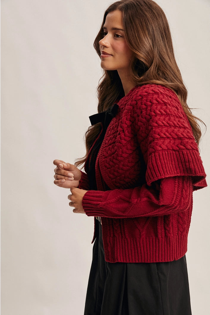 Woman wearing a red knitted cardigan over a black top against a plain background
