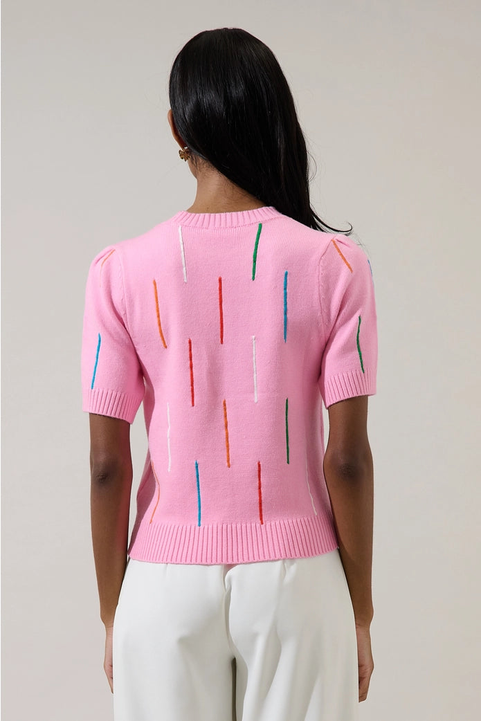 Person wearing a pink sweater with colorful vertical stripes on a plain background