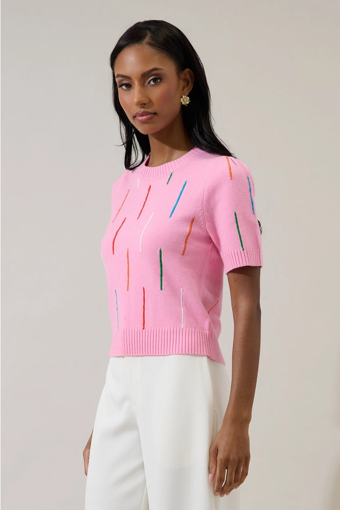 Woman wearing a pink sweater with colorful accents on a plain background