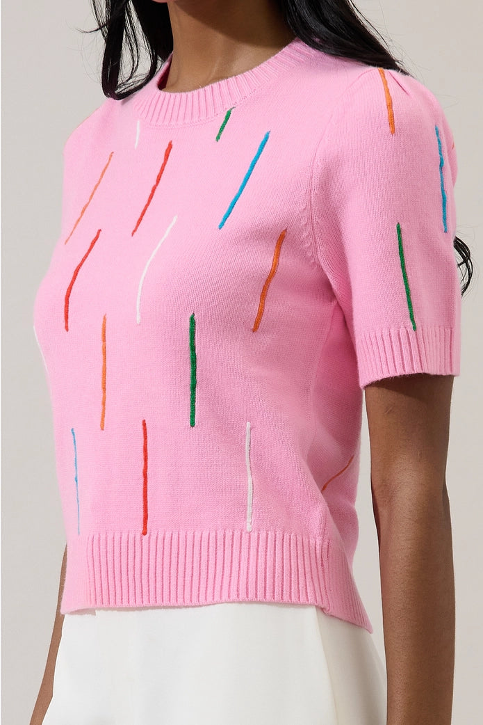 Pink sweater with colorful vertical stripes worn by a person on a plain background