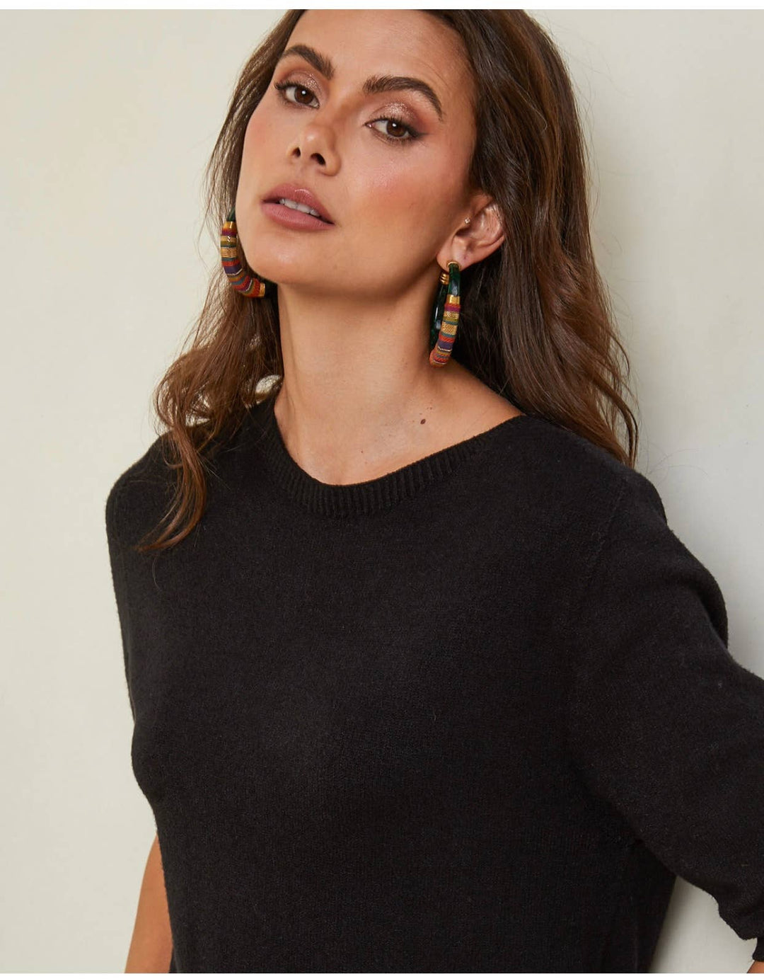 Woman wearing a black sweater with colorful earrings against a neutral background