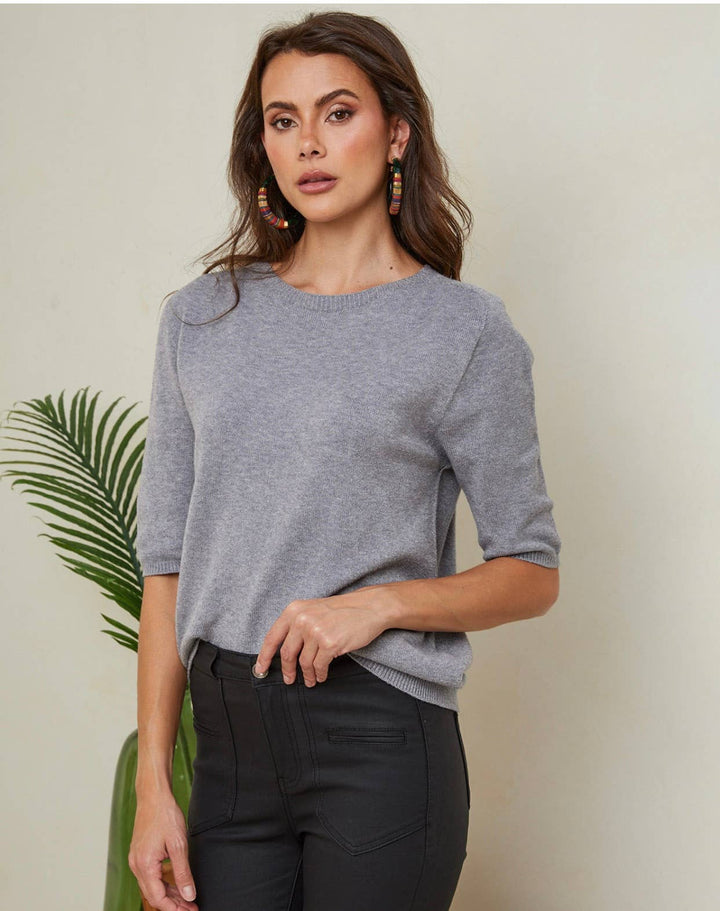 Woman wearing a gray sweater and black pants against a neutral background