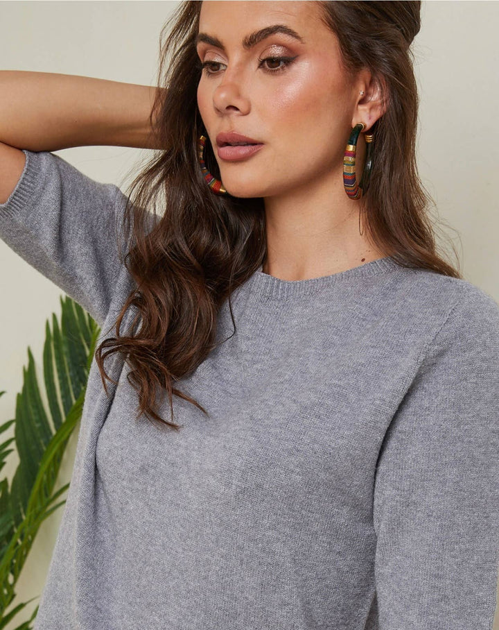 Woman wearing a gray sweater with colorful earrings against a neutral background