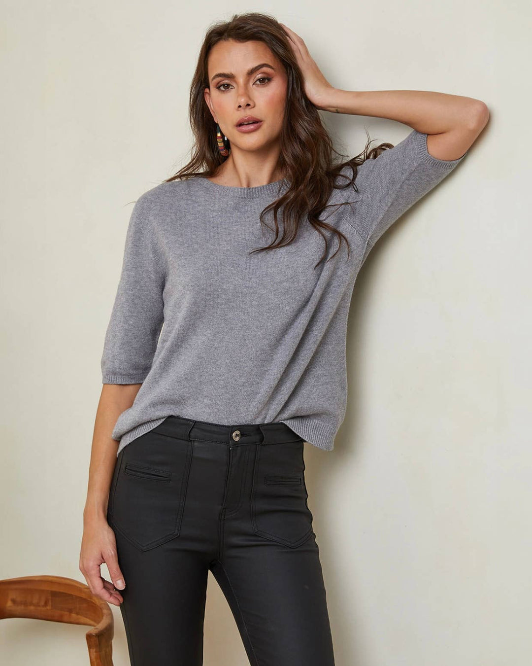 Woman wearing a gray sweater and black pants against a plain background