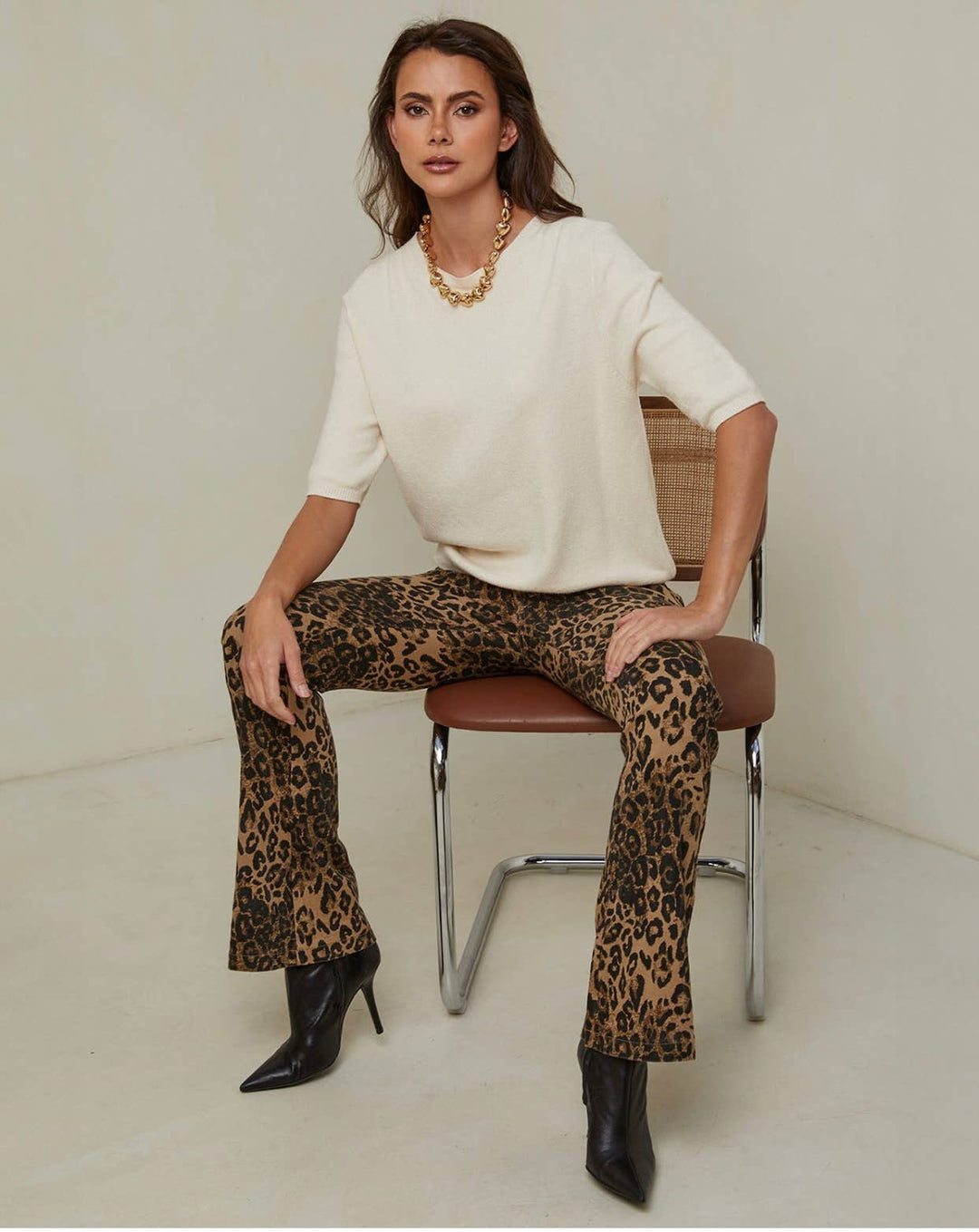 Woman sitting on a chair wearing a white top and leopard print pants.