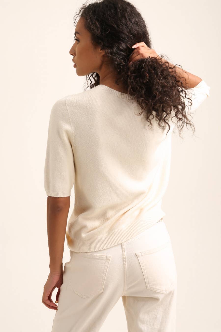 Woman wearing a cream-colored sweater and pants against a white background