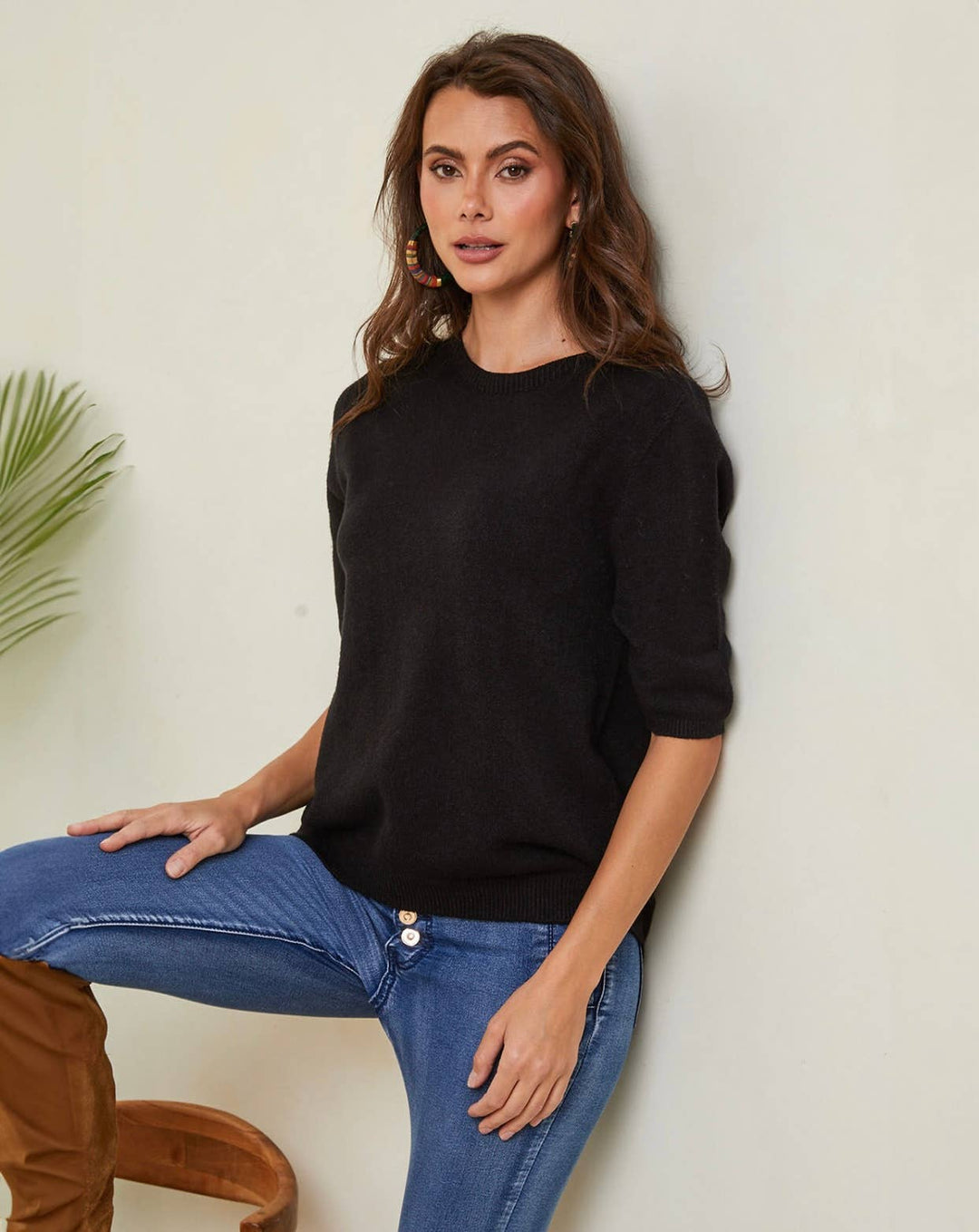 Woman wearing a black sweater and blue jeans against a neutral background