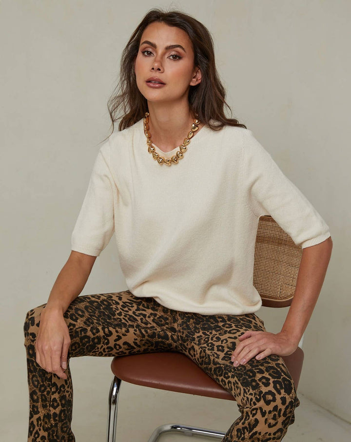 Woman wearing a white sweater and leopard print pants sitting on a chair.