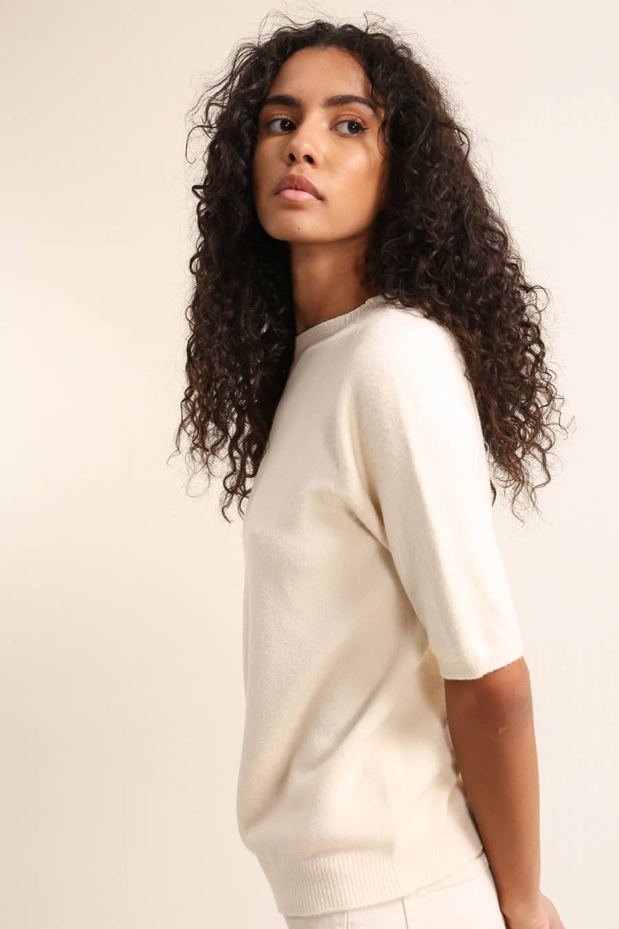 Woman wearing a cream-colored sweater against a plain background