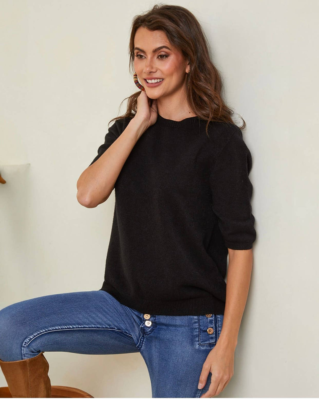Woman wearing a black sweater and blue jeans against a plain background
