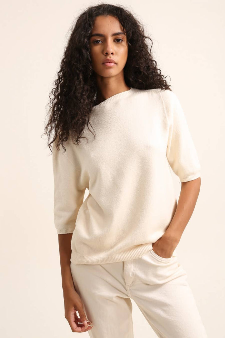 Woman wearing a cream-colored outfit against a plain background