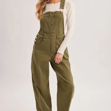A model wearing olive green wide-leg denim overalls over a cream long-sleeve shirt, shown from the waist down against a light gray studio background.