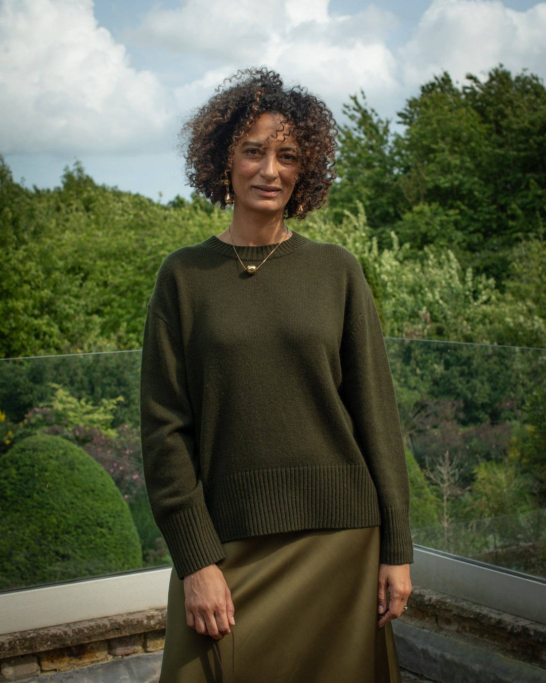 Woman wearing a green sweater and skirt standing outdoors with trees in the background