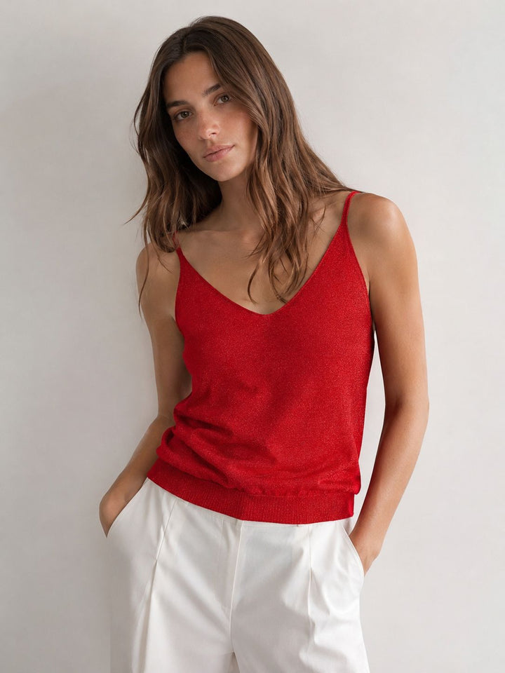 Woman wearing a red tank top and white pants against a plain background