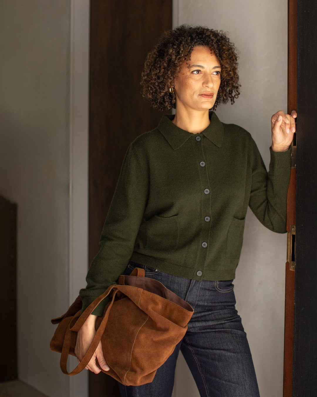 Woman in a green shirt holding a brown bag, standing in a doorway.