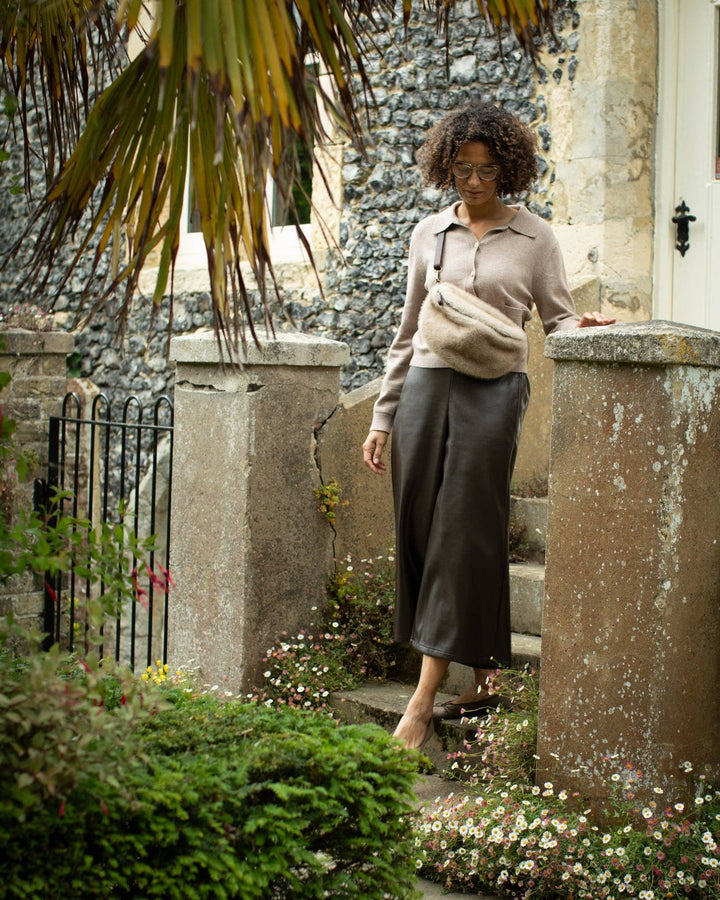 Woman walking outdoors near a stone building with plants and flowers around.