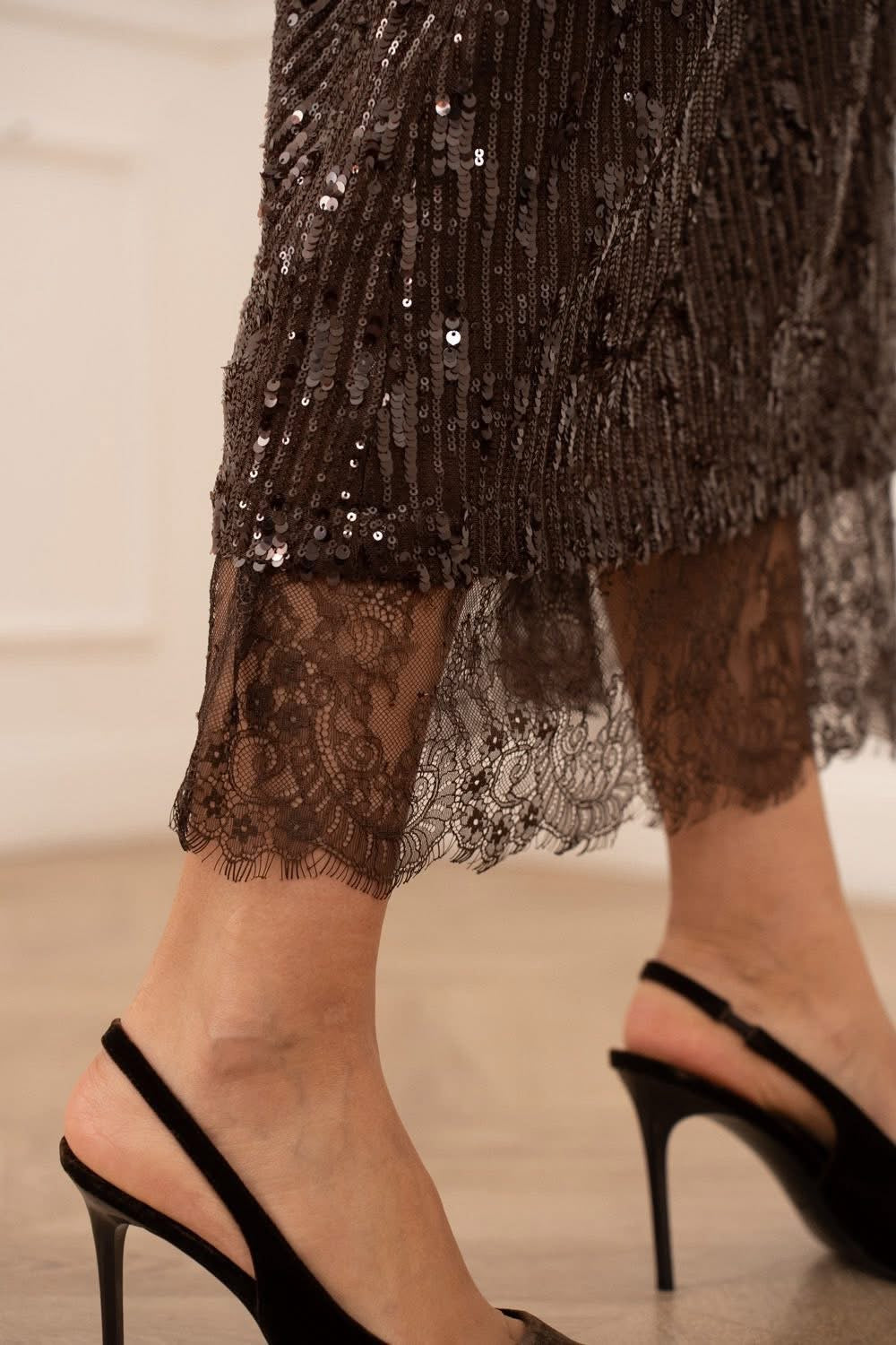 Close-up of a person wearing a sequined skirt and black high-heeled shoes.