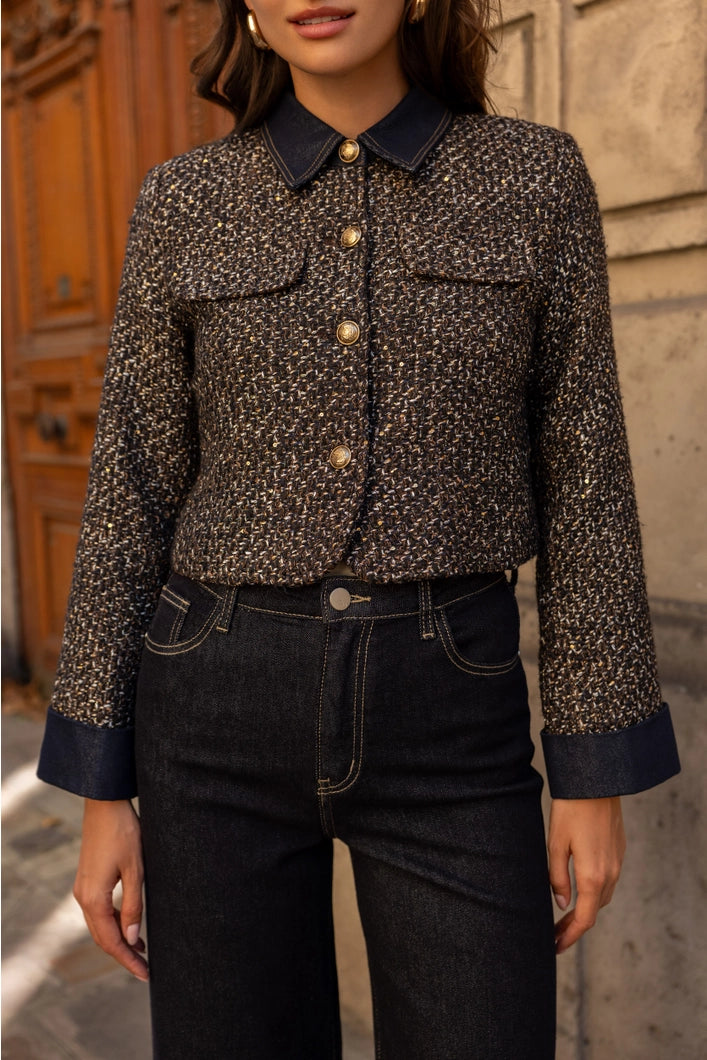 Person wearing a patterned jacket and dark jeans against a stone wall.