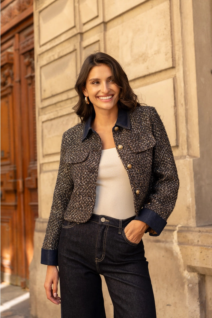 Woman wearing a patterned jacket and white top standing against a stone wall.