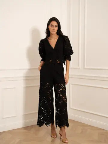 Woman wearing a black lace jumpsuit standing against a white wall.