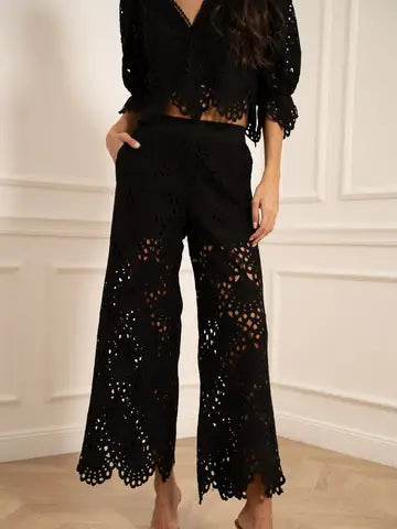 Person wearing a black lace outfit against a white wall.