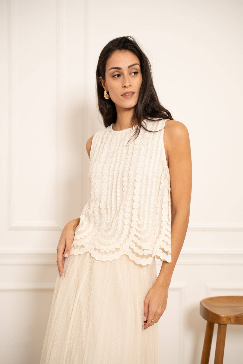 Woman wearing a white sleeveless top with lace details against a plain background