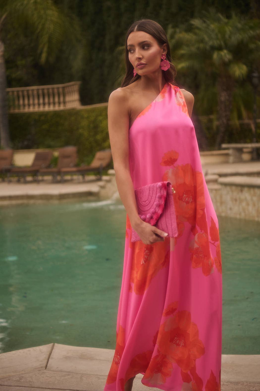 Woman in a pink floral dress standing by a pool with palm trees in the background