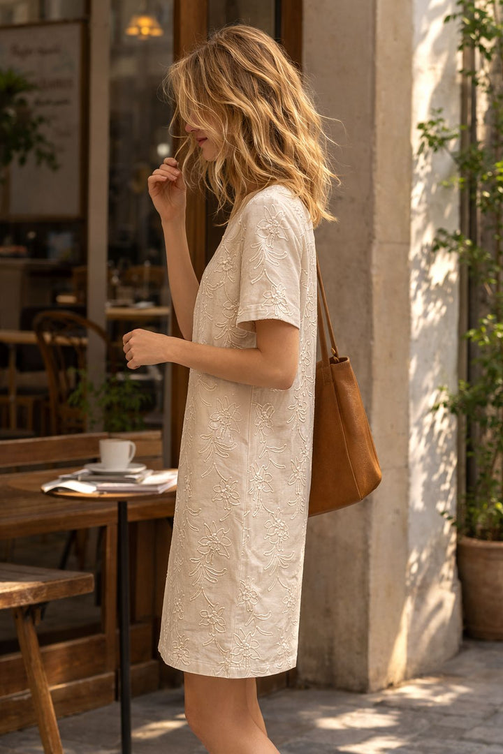 Woman in a white dress holding a brown bag on a street.