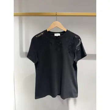 Black t-shirt with lace details on a hanger against a neutral background