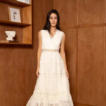Woman in a white dress standing against a wooden wall.