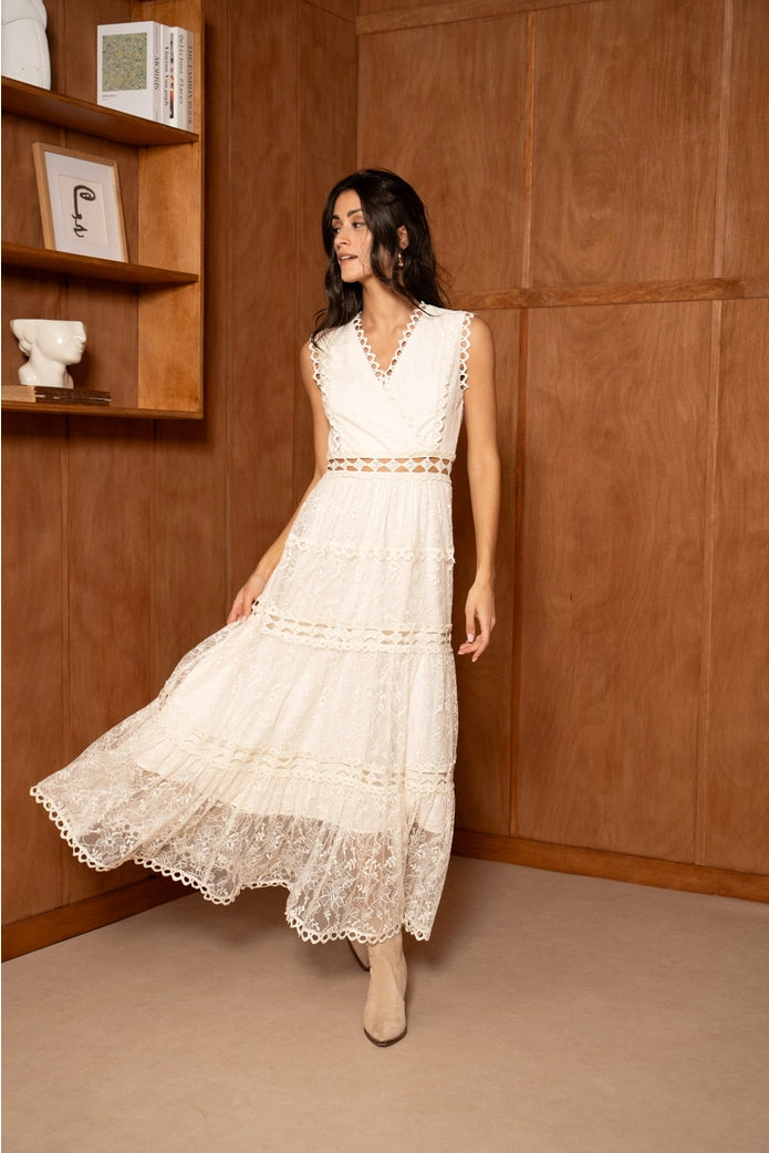 Woman in a white lace dress standing in a room with wooden walls.